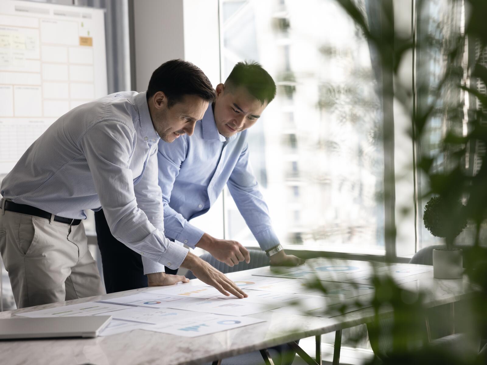 Two colleagues leaning over printed charts together, one pointing at the data