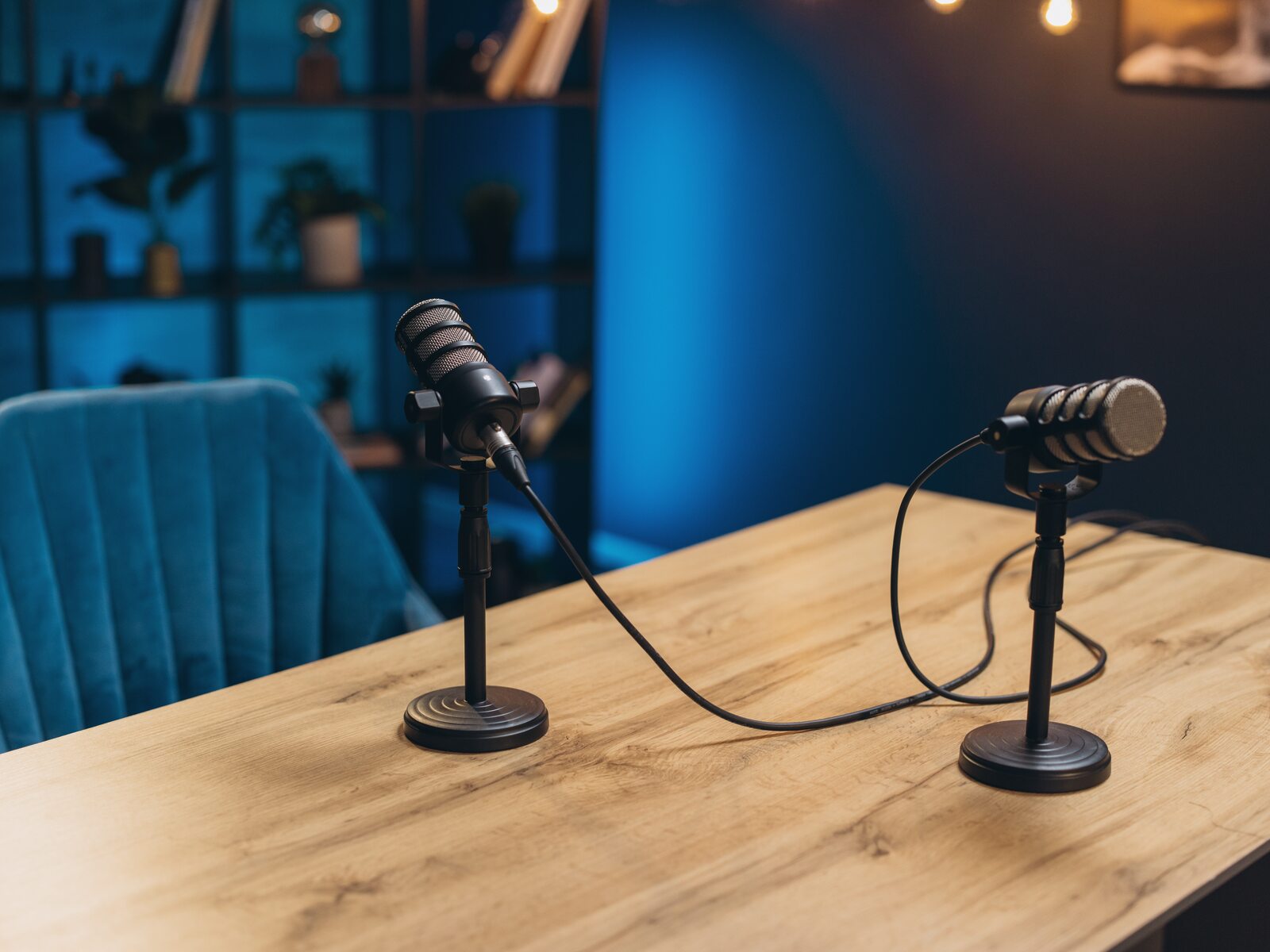 A podcast microphone on a boom arm over a worn wood desk, an empty leather guest chair waiting behind it