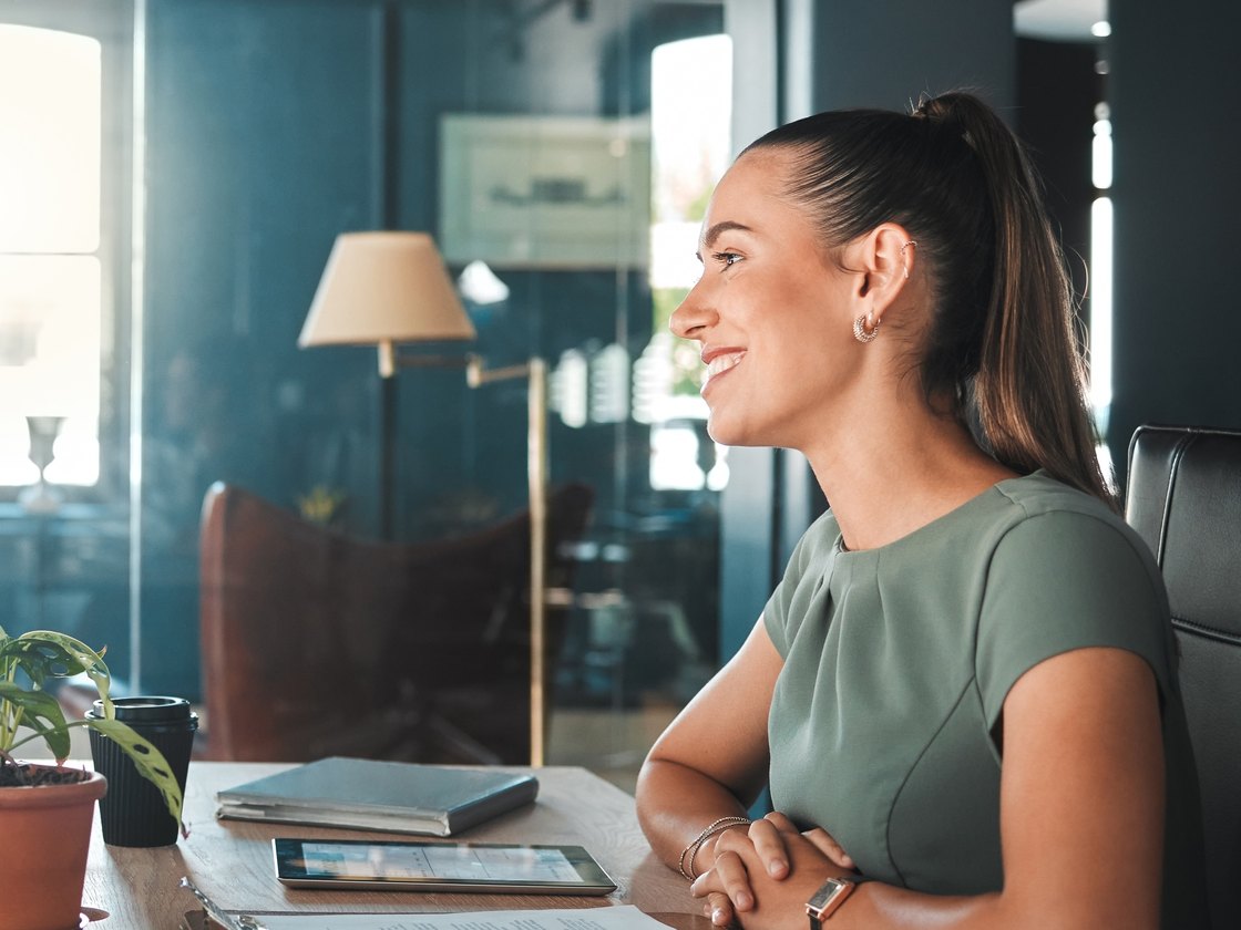 A hiring conversation in a glass-walled office: a candidate seated at a meeting table, listening.